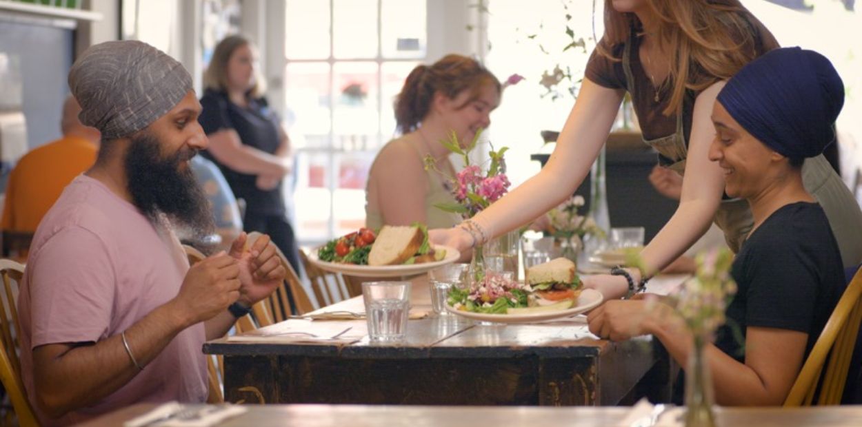 Couple sits at a table in a busy restaurant and food is being delivered to them by a waitress.